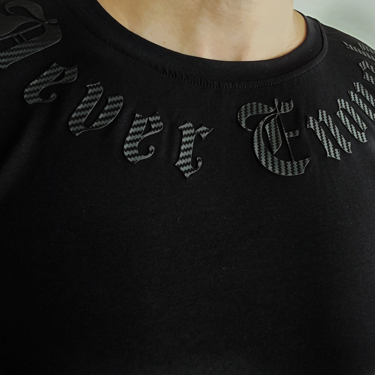 Gros plan des lettres Never enough noires autour de l'encolure du T-shirt Gold line