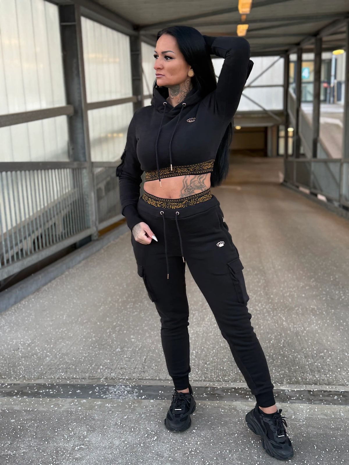 Model im schwarzen MVL Meander Damen-Trainingsanzug mit Cropped Hoodie auf einer Fußgängerbrücke