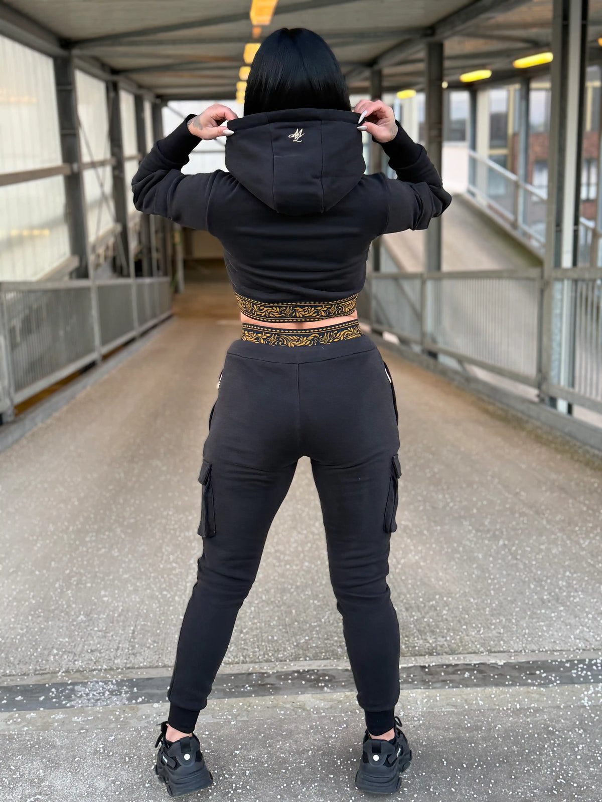 Rückseite des cropped MVL Meander Damen-Hoodies mit aufgesetzter Kapuze, Model auf einer Fußgängerbrücke