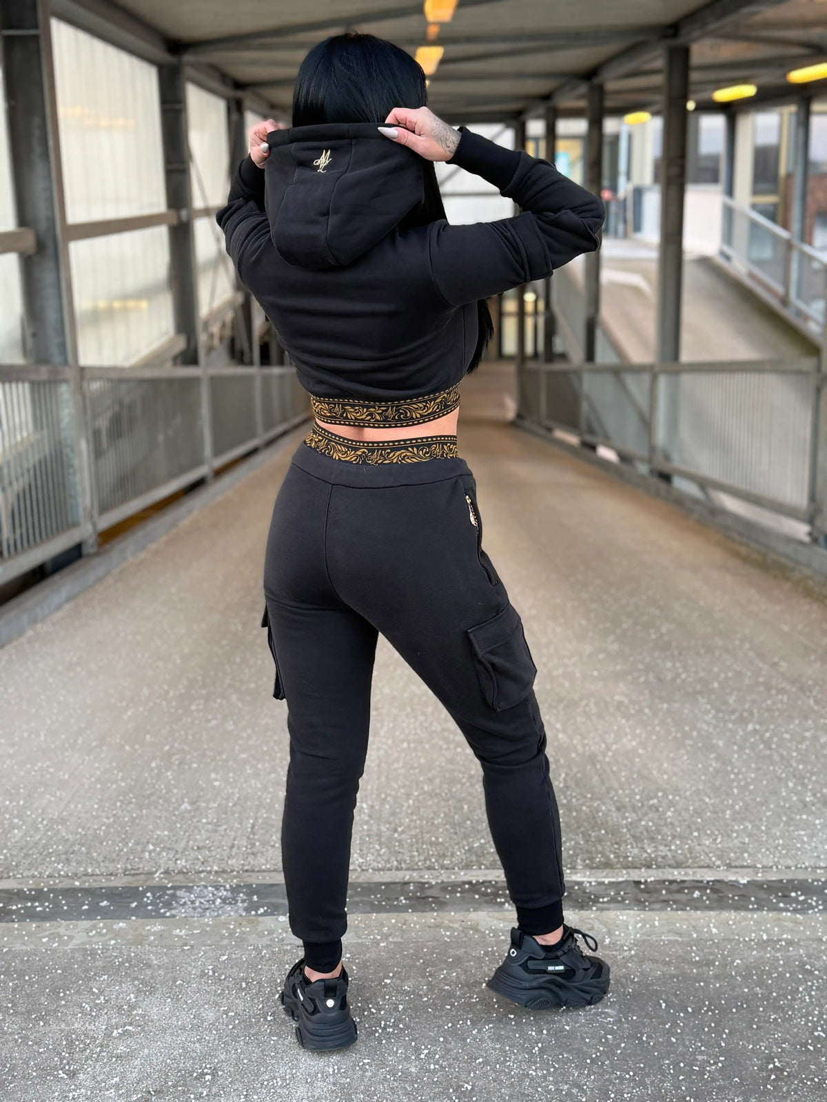 Model zeigt die Rückseite des MVL Meander Damen-Trainingsanzugs mit den Händen an der Kapuze