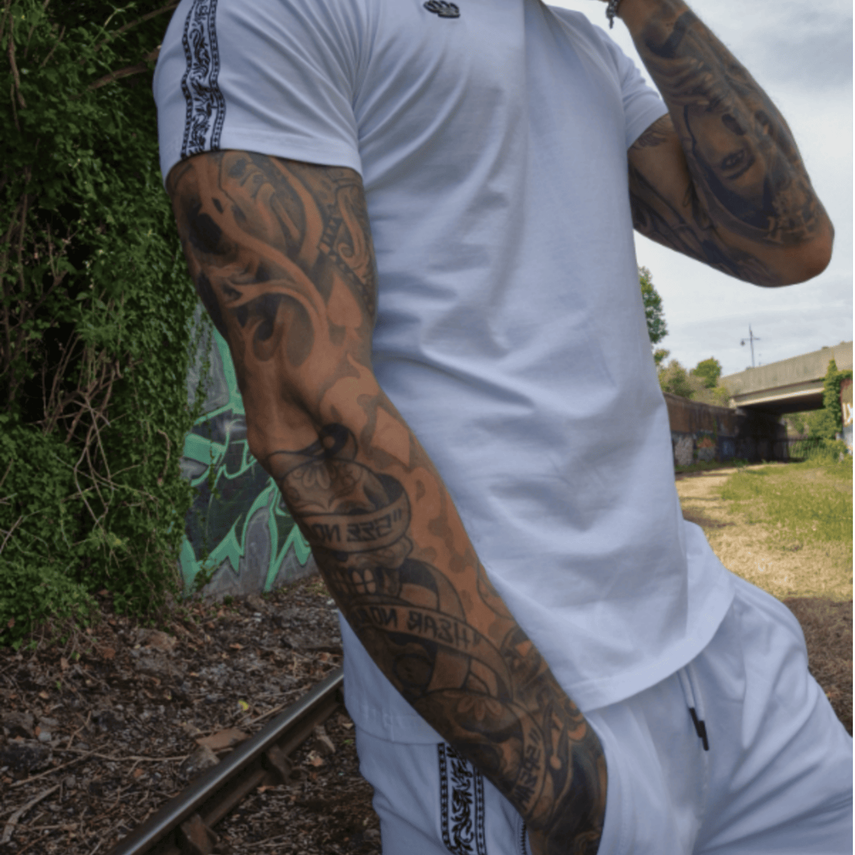 Modello con T-shirt MVL bianca e shorts Meander bianchi vicino a binari con graffiti