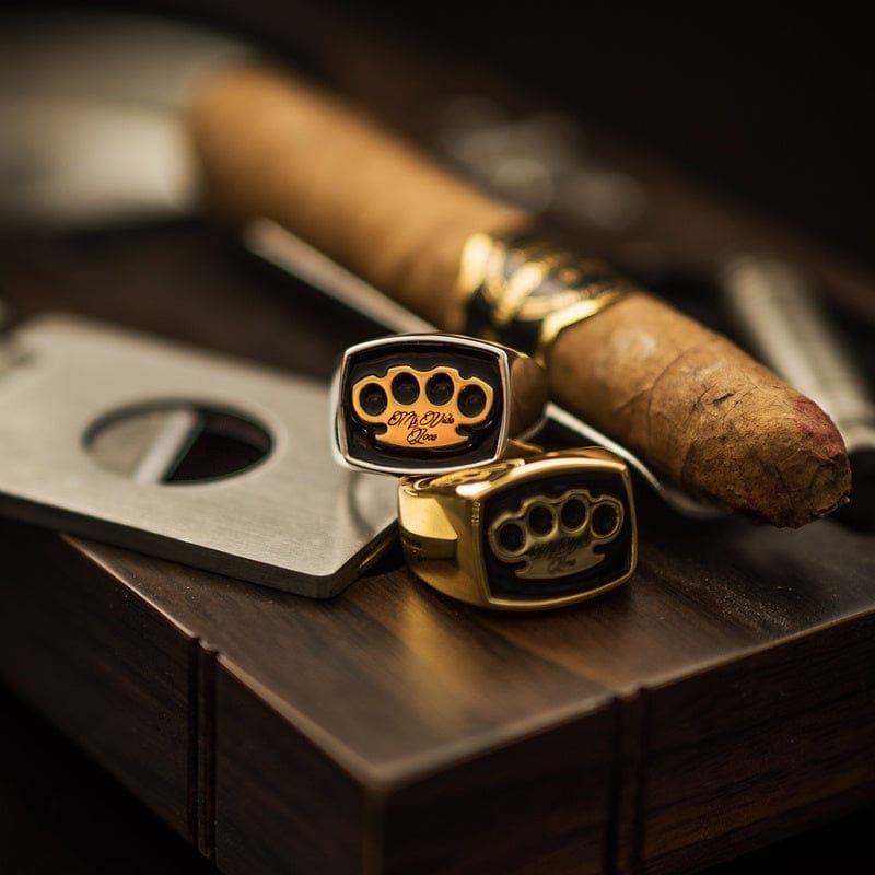 Silver and gold MVL signet ring next to a cigar and cigar cutter on wood