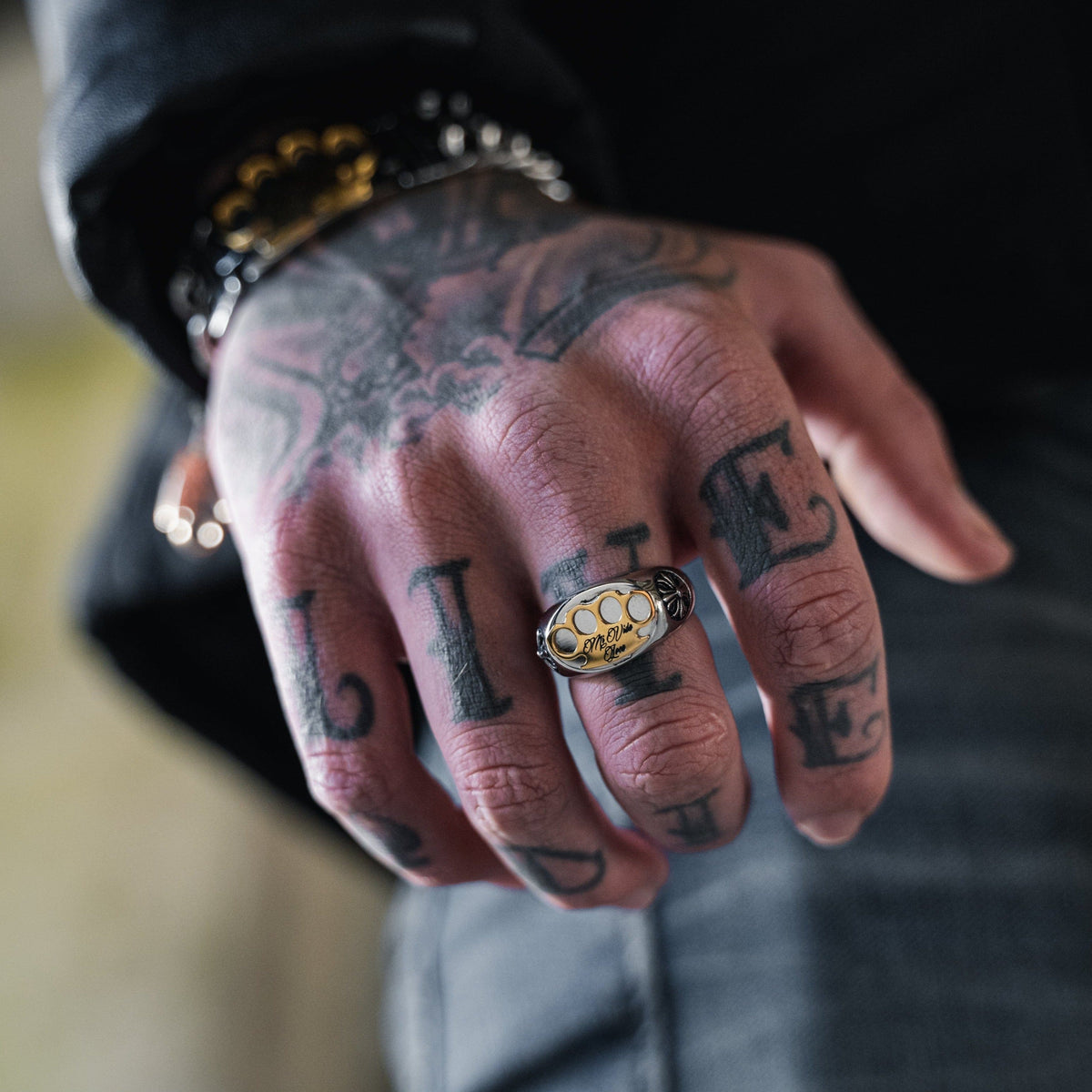 Bague MVL Logo argentée au doigt d'une main tatouée, gros plan